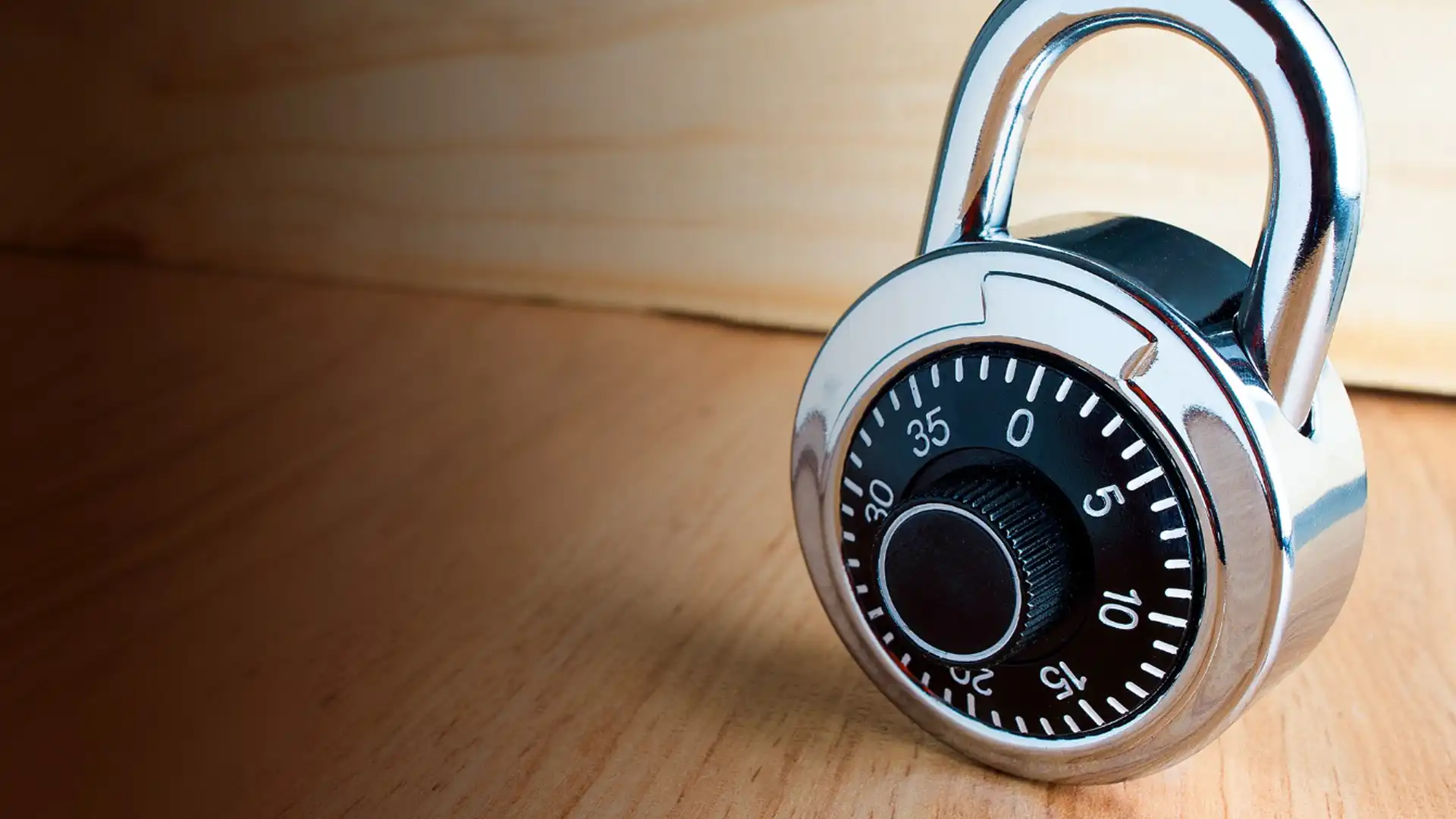 Metal combination padlock with a dial resting on a wooden surface, symbolizing security and protection.